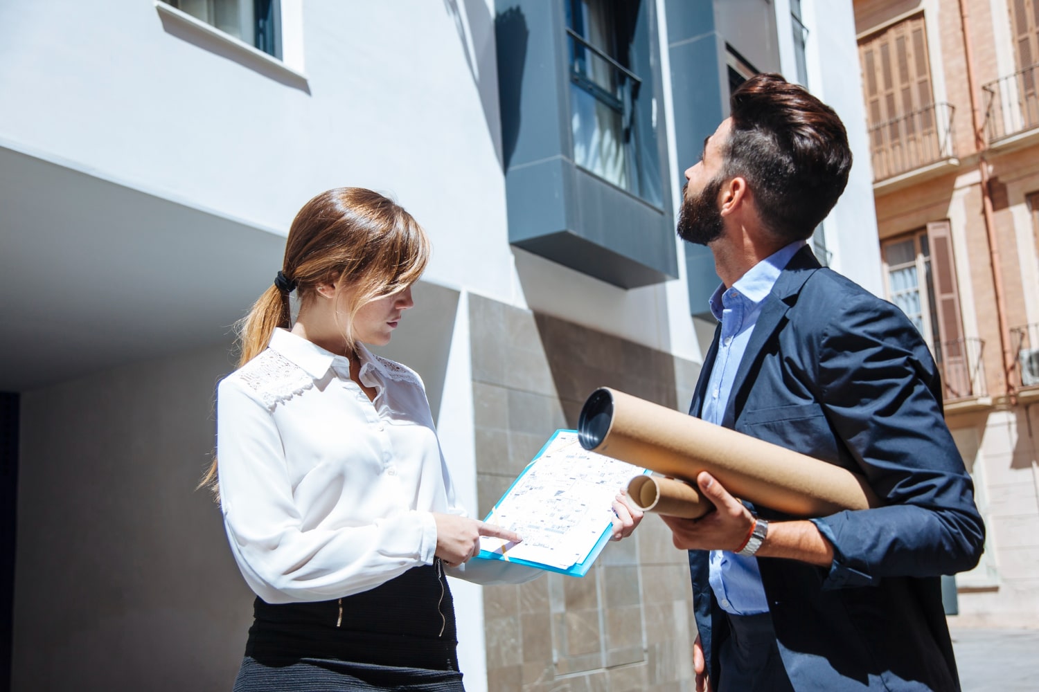 two real estate agents a man and a woman holding a piece of paper In front of a building